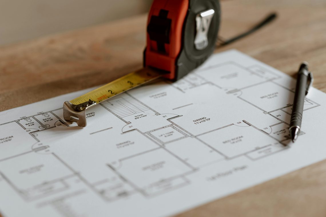 floor plan, tape measure, and gray pen on wooden table